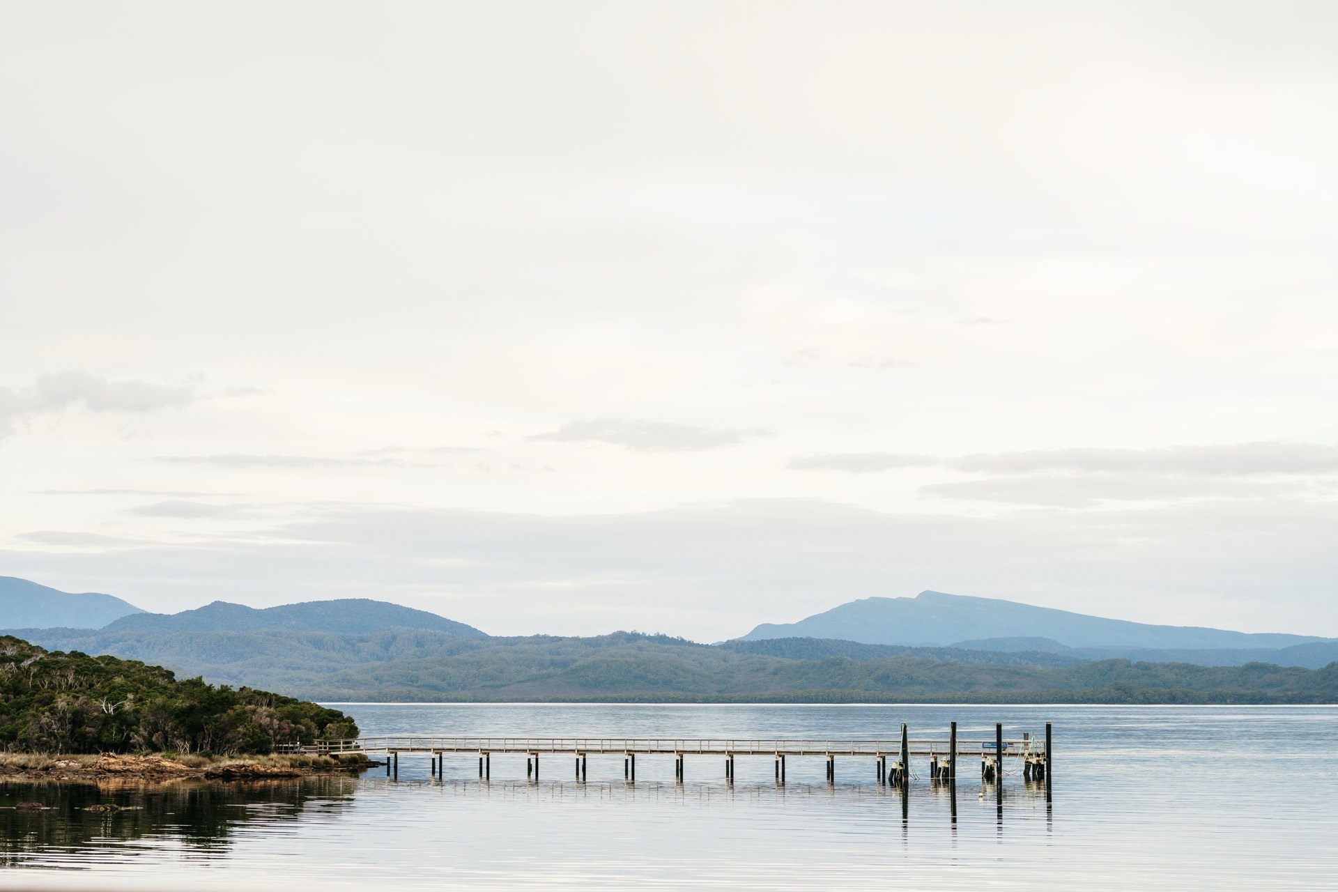 A long wooden jetty on still water below forested hills near Strahan