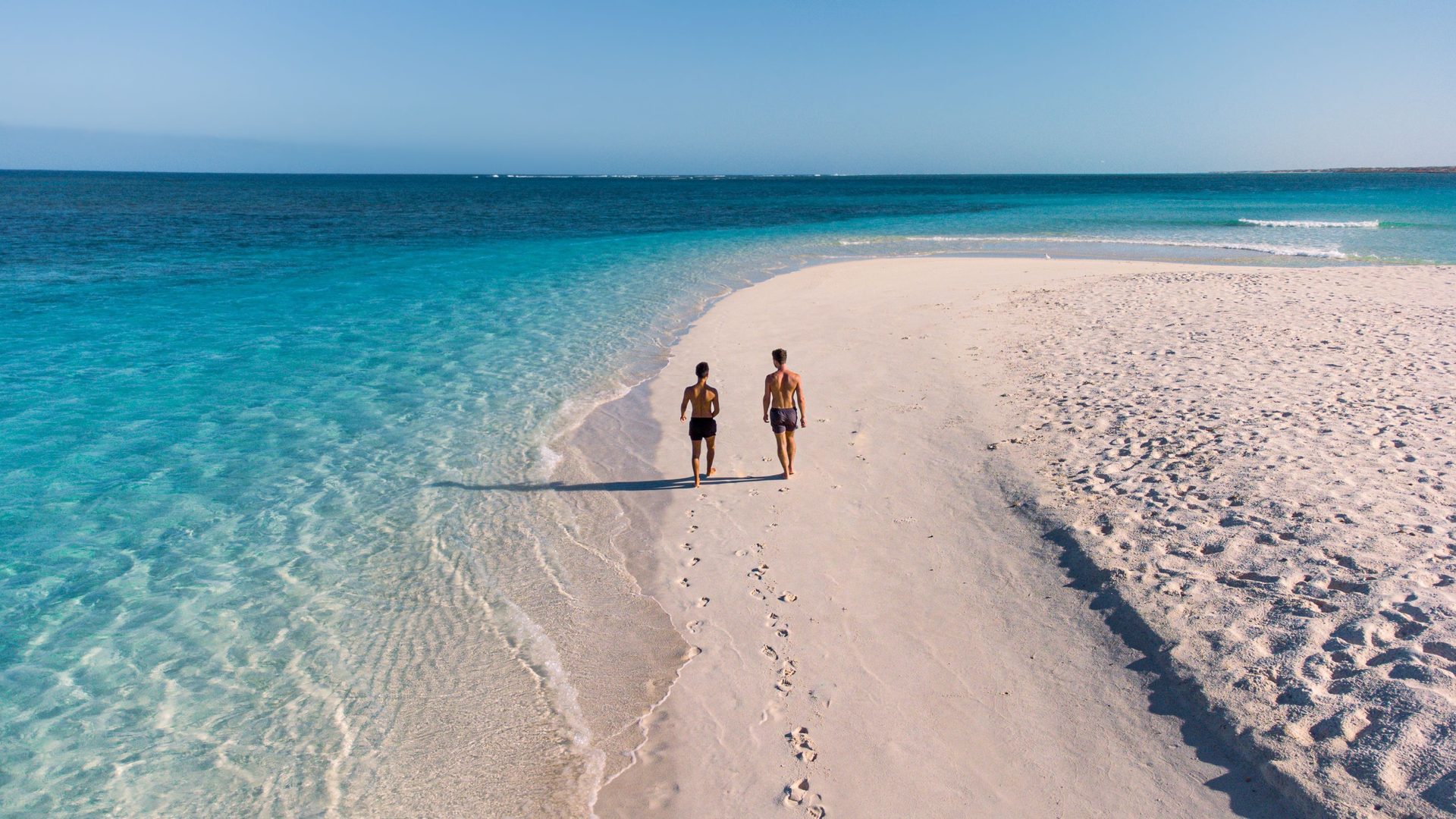 Two walkers on white sand beside clear turquoise water at Turquoise Bay near Exmouth